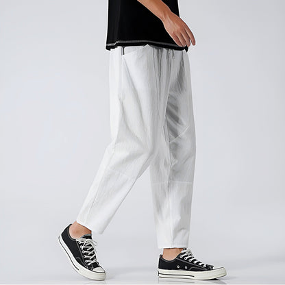 Person wearing white pants and black sneakers on a plain background