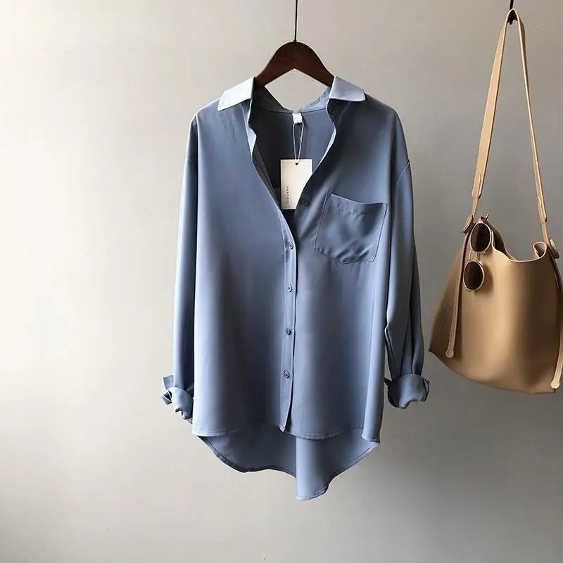 Blue shirt on a hanger next to a beige handbag against a neutral background