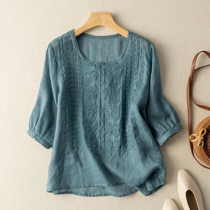 Blue embroidered blouse on a wooden hanger with a beige background