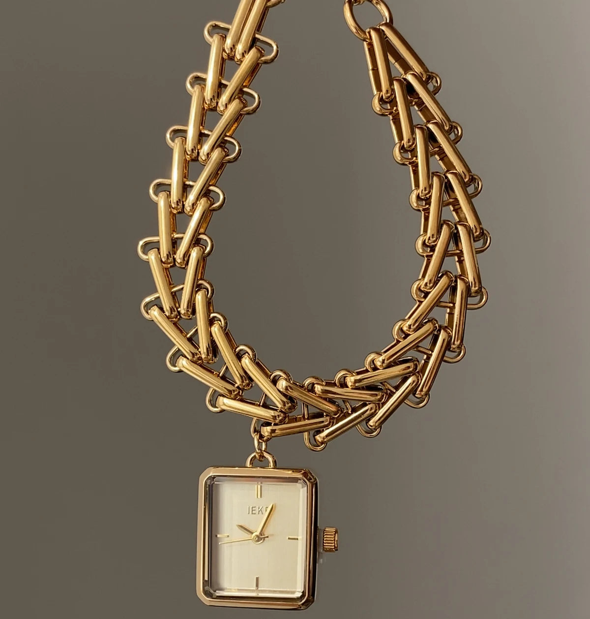 Gold chain watch with a square face on a gray background