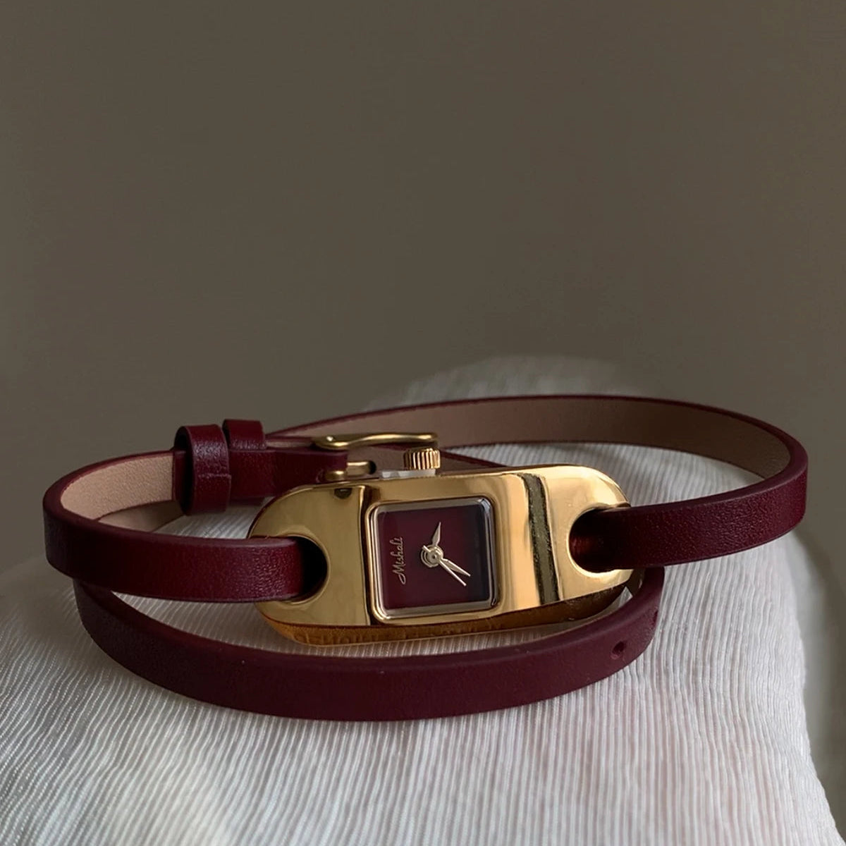 Brown leather bracelet with gold clasp on a light gray surface.
